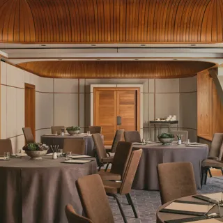 Boardroom setup with grey tablecloth, neutral chairs, succulents, and colourful abstract window panels under a curved wooden ceiling.