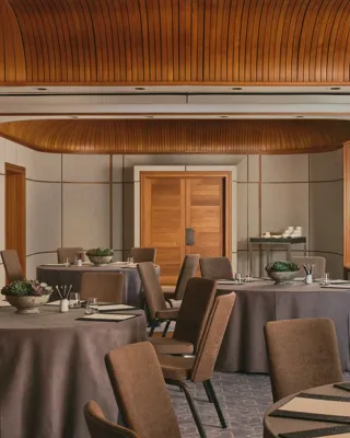 Boardroom setup with grey tablecloth, neutral chairs, succulents, and colourful abstract window panels under a curved wooden ceiling.