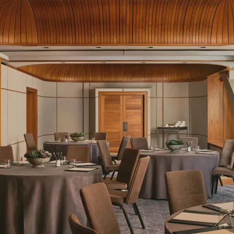 Boardroom setup with grey tablecloth, neutral chairs, succulents, and colourful abstract window panels under a curved wooden ceiling.