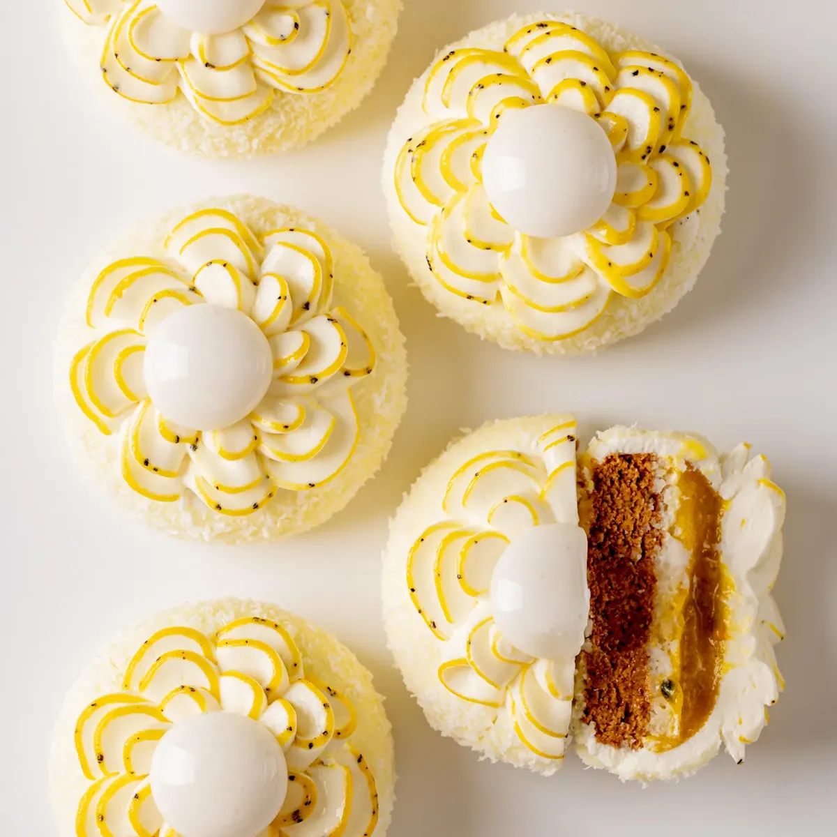Coconut and passion fruit pastries with piped cream petals and glossy domes, one sliced to reveal layered sponge and fruit filling