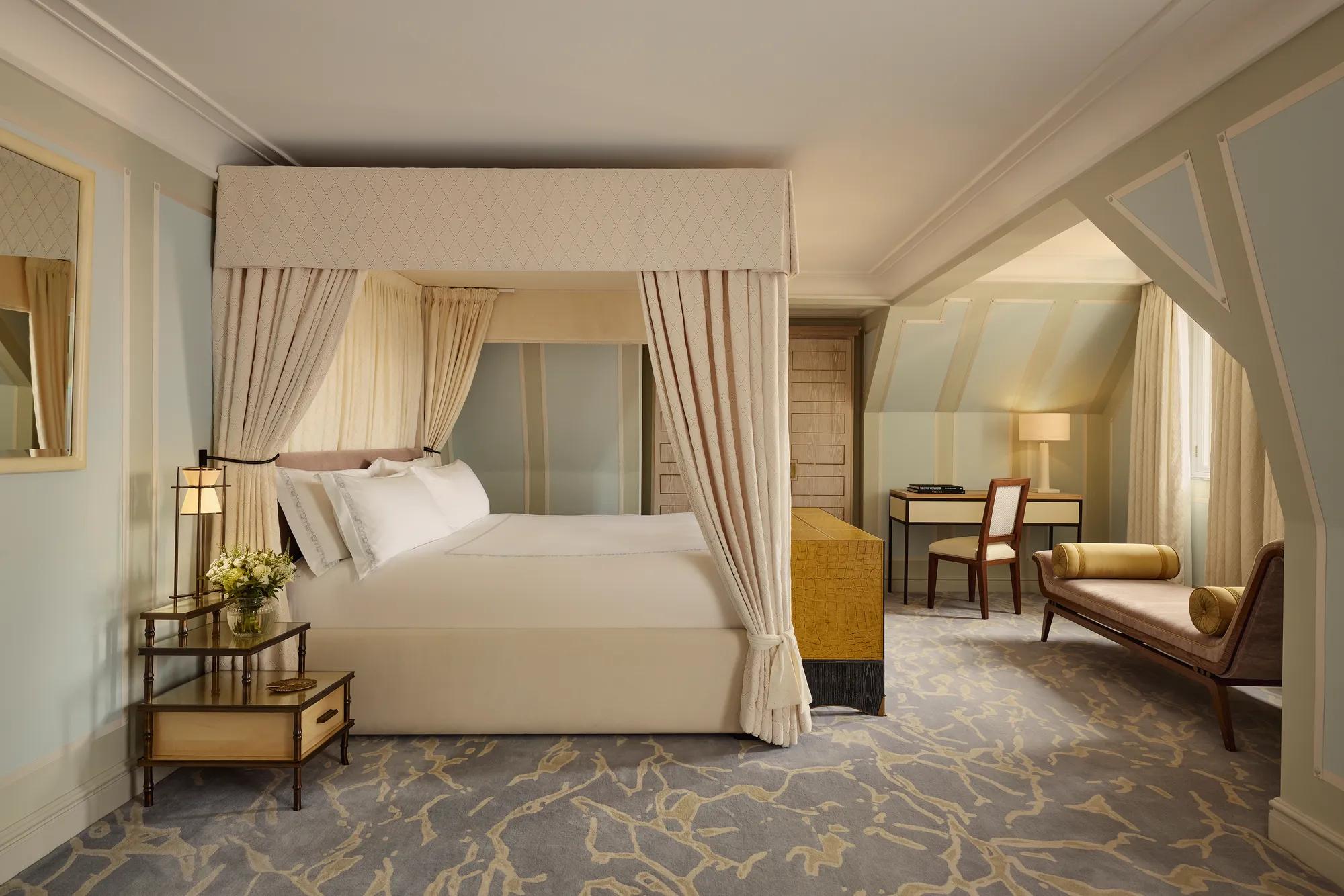 Spacious bedroom with four-poster bed, chaise longue, desk area, and soft pastel decor.
