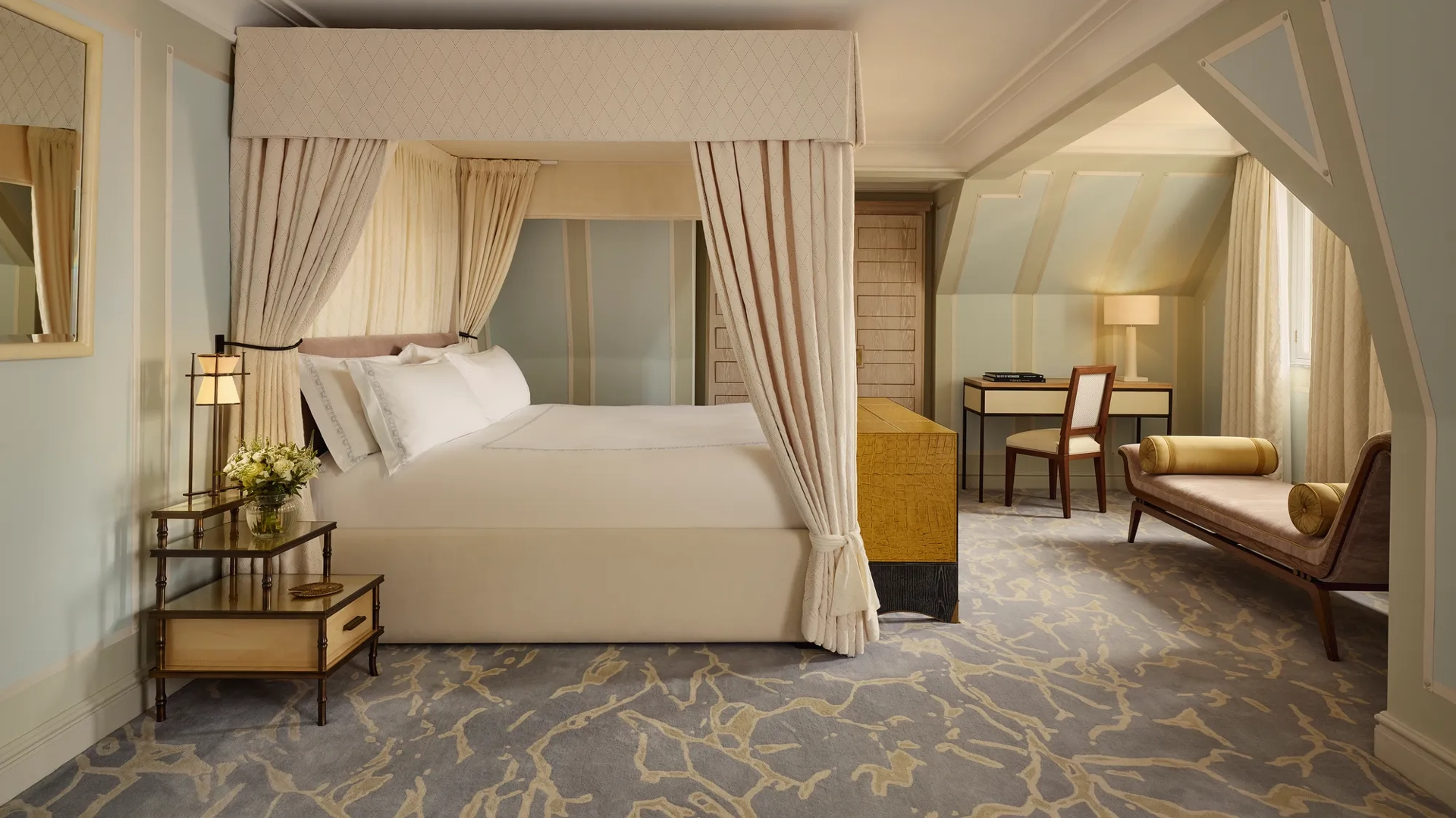 Spacious bedroom with four-poster bed, chaise longue, desk area, and soft pastel decor.