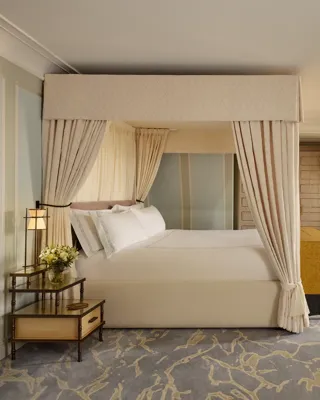 Spacious bedroom with four-poster bed, chaise longue, desk area, and soft pastel decor.