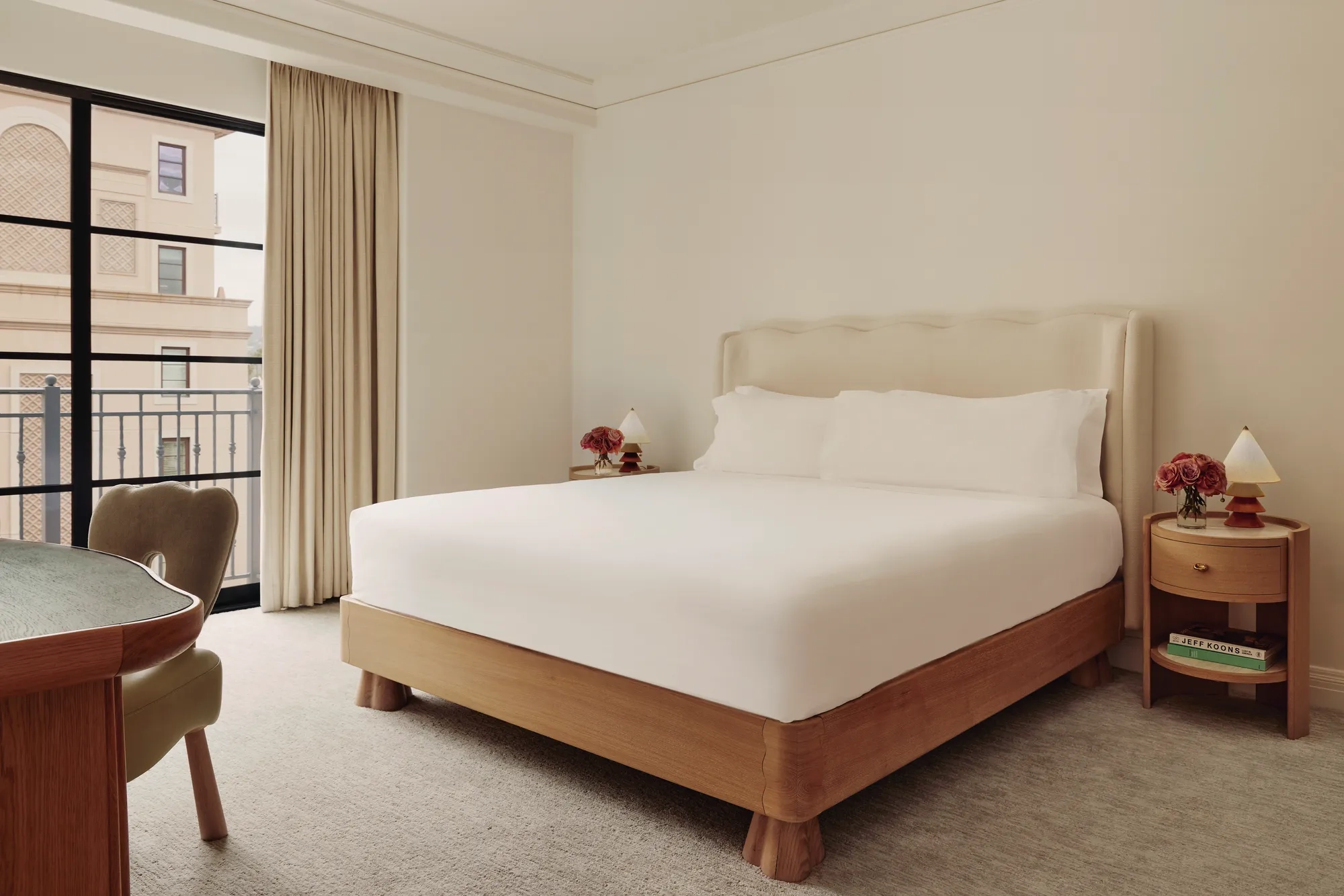Calm bedroom with upholstered king bed, wooden nightstands, desk chair, and window to a Juliet balcony.