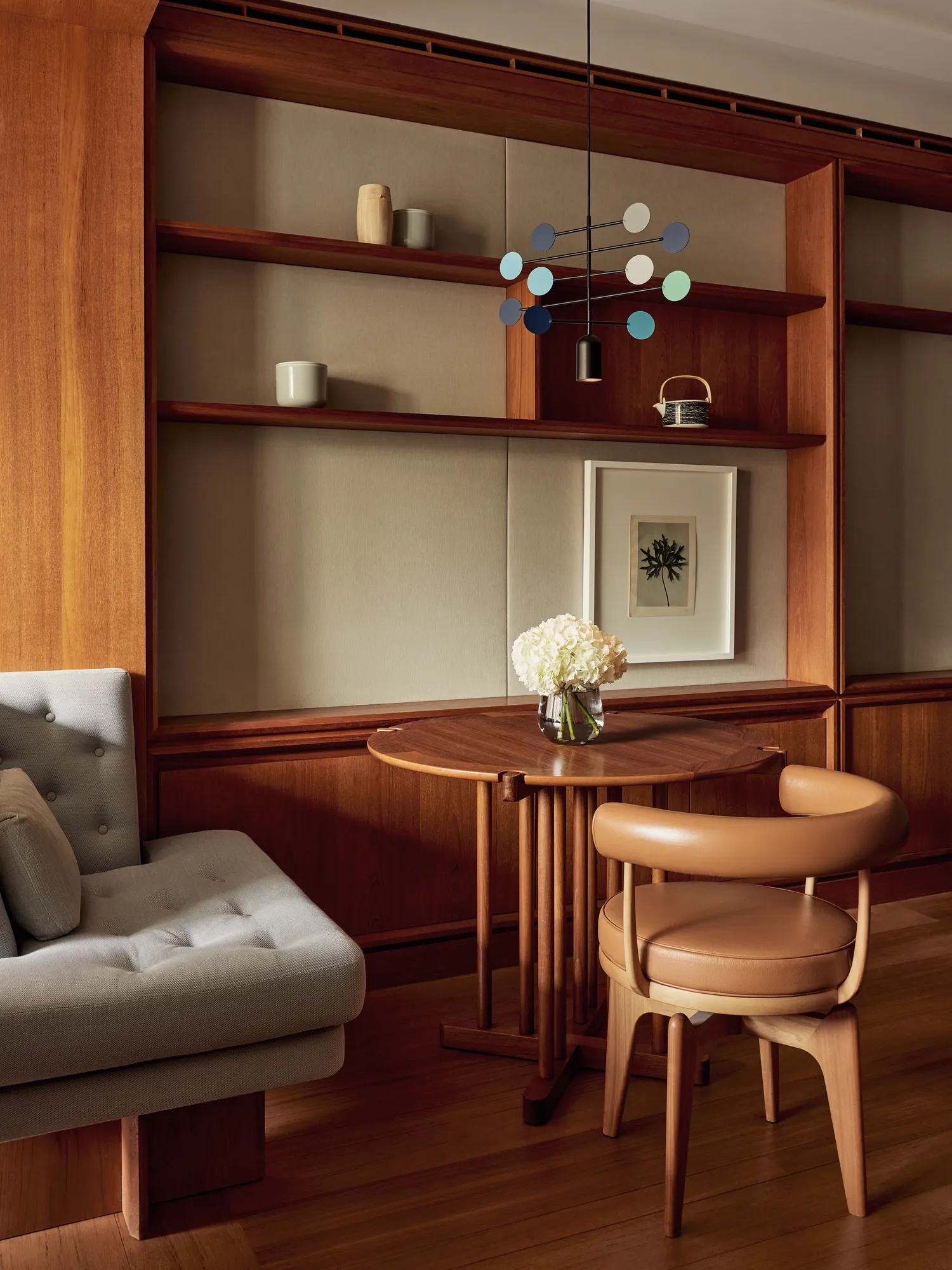 Small wooden dining table with leather chair, cushioned bench, and shelves decorated with ceramics and a framed print.
