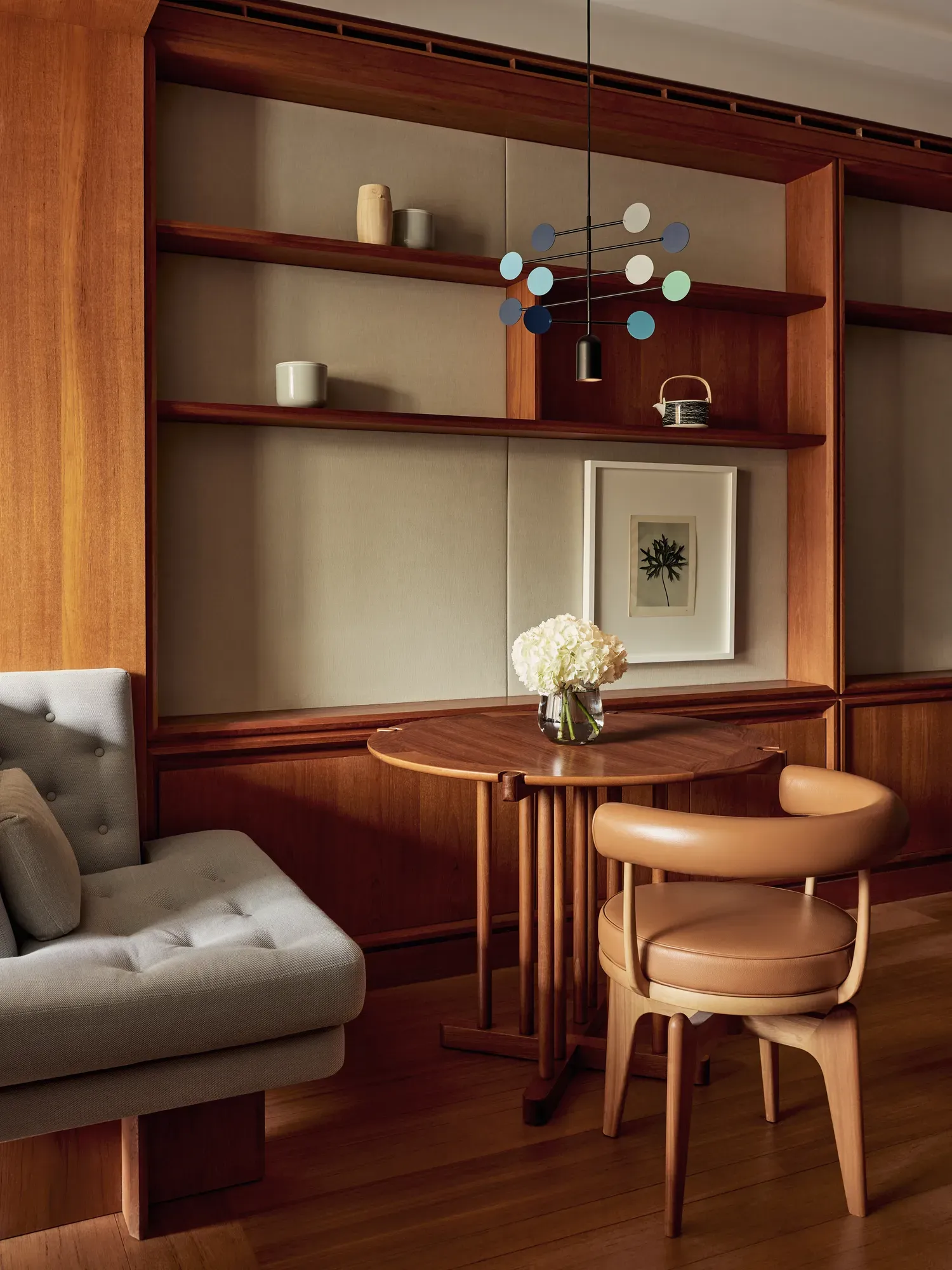 Small wooden dining table with leather chair, cushioned bench, and shelves decorated with ceramics and a framed print.
