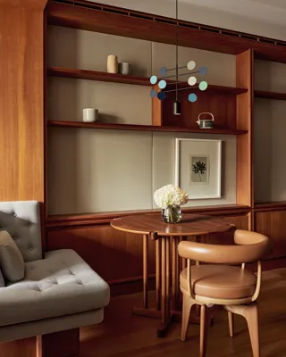 Small wooden dining table with leather chair, cushioned bench, and shelves decorated with ceramics and a framed print.