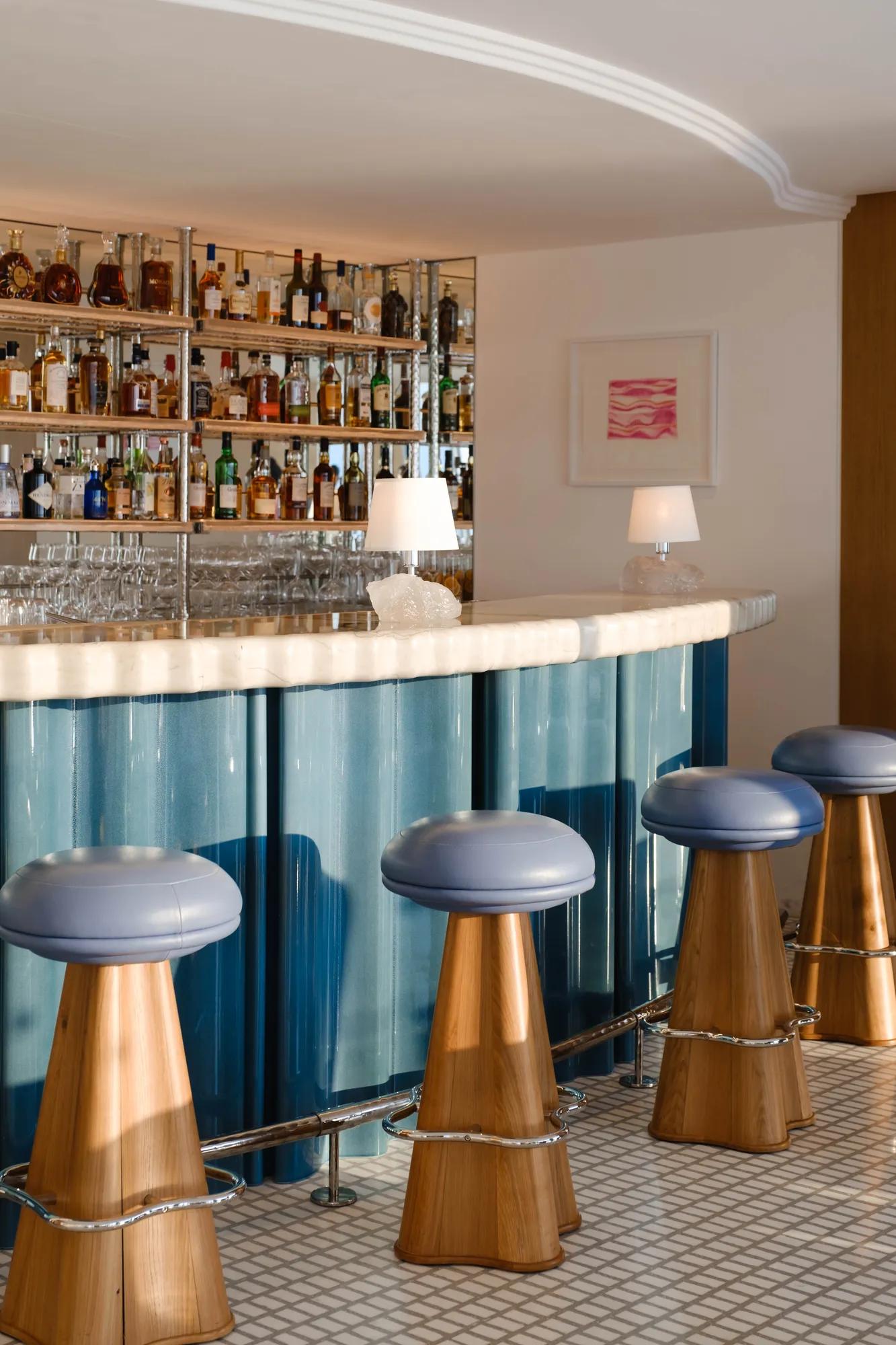 Chic bar with blue leather stools, marble counter, mirrored shelves filled with bottles, and soft ambient lighting.