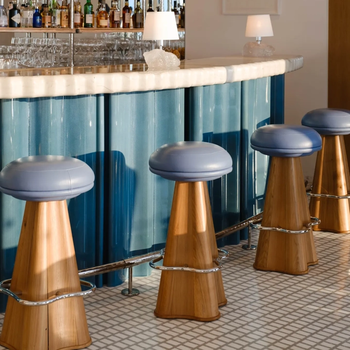 Bar élégant avec tabourets en cuir bleu, comptoir en marbre, étagères miroirs garnies de bouteilles et éclairage doux.