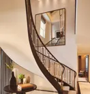 Curved staircase with dark wood railing in a marble-floored suite, beside a sculptural table and large wall mirror.