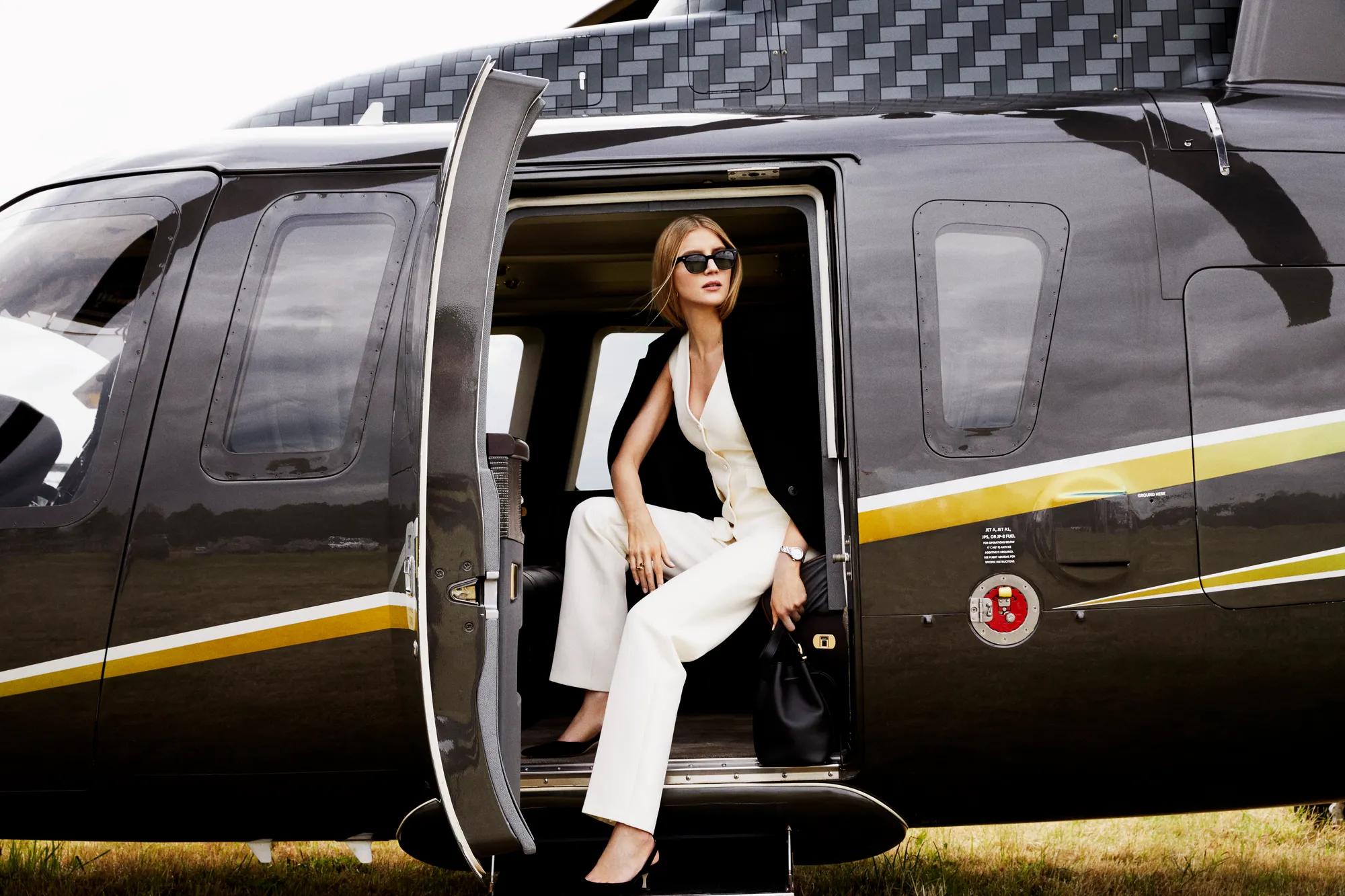 A young woman climbing out of a helicopter onto a tarmac, with the aircraft’s door open behind her.