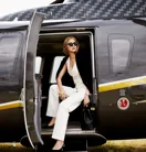 A young woman climbing out of a helicopter onto a tarmac, with the aircraft’s door open behind her.