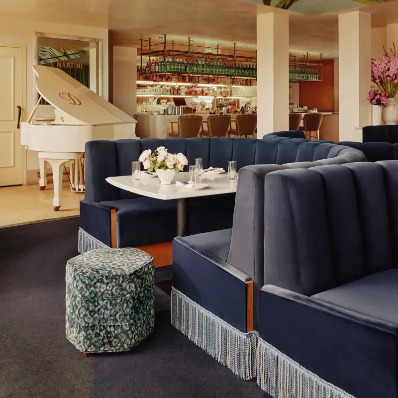 Dante Beverly Hills restaurant and rooftop with navy velvet banquettes and fringe, white grand piano, and a colorful ceiling mural near the bar.