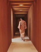 A woman wearing a patterned kimono walks down a softly lit wooden corridor with a geometric ceiling at The Maybourne Riviera.