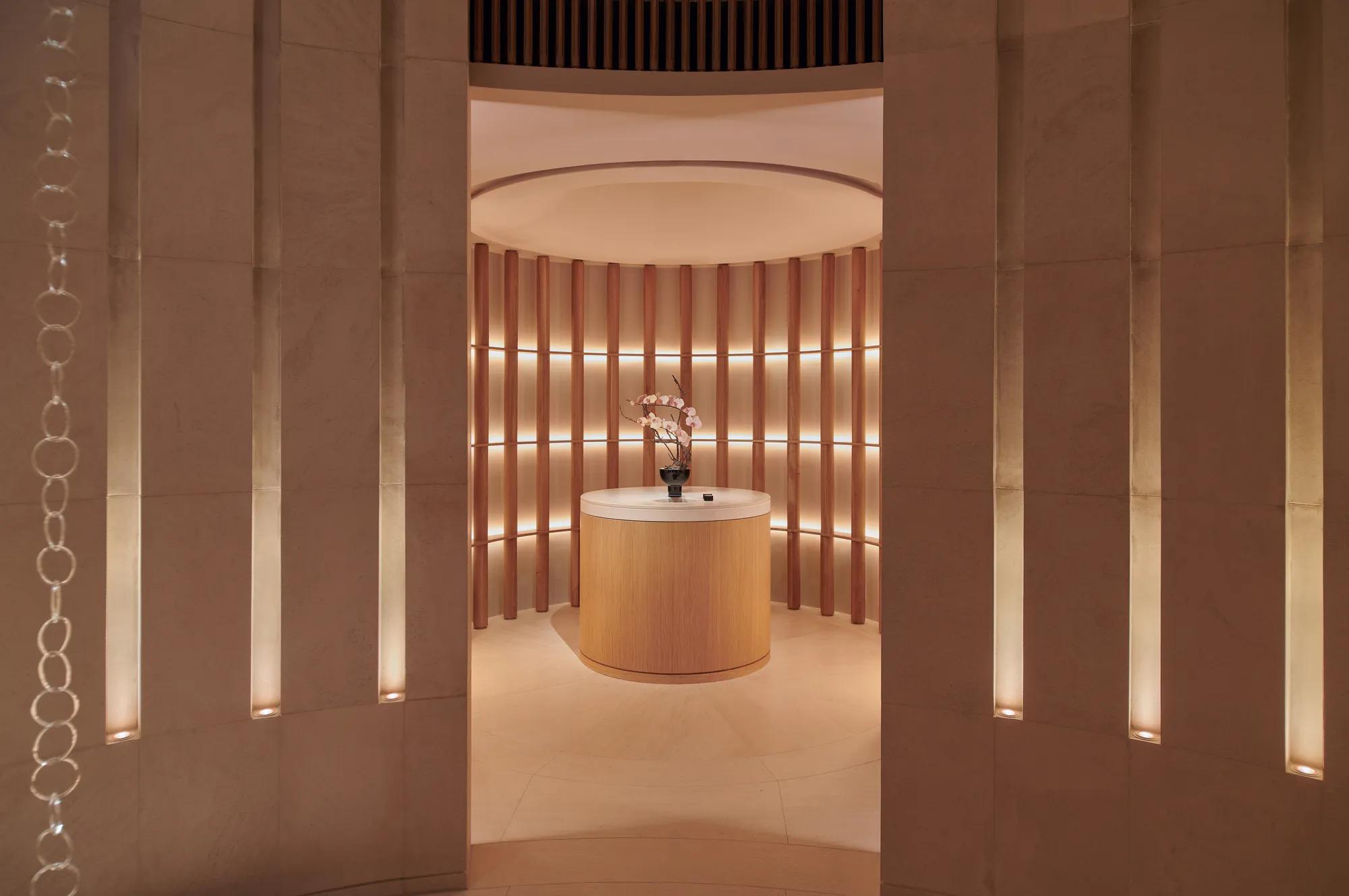 Softly lit circular alcove with a round wooden table holding a vase of orchids, surrounded by vertical wooden slats and warm ambient lighting at The Maybourne Riviera.