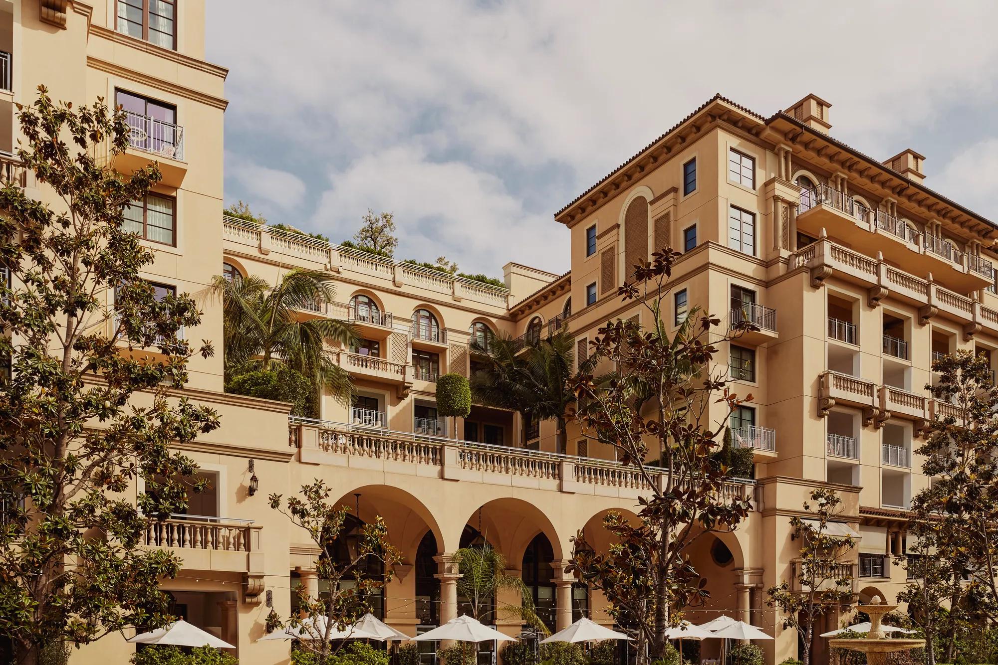 Arched terrace of The Maybourne Beverly Hills facing Beverly Canon Gardens, with palms and white umbrellas below.