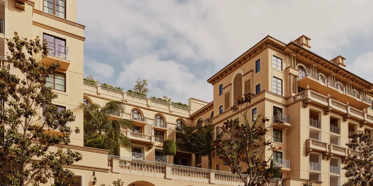 Arched terrace of The Maybourne Beverly Hills facing Beverly Canon Gardens, with palms and white umbrellas below.