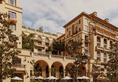 Arched terrace of The Maybourne Beverly Hills facing Beverly Canon Gardens, with palms and white umbrellas below.