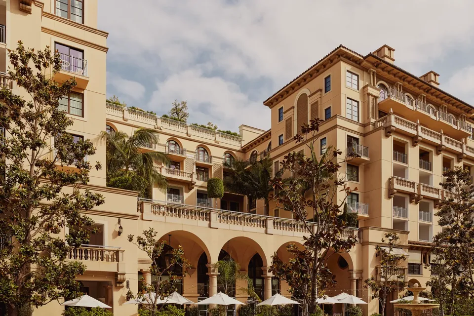 Arched terrace of The Maybourne Beverly Hills facing Beverly Canon Gardens, with palms and white umbrellas below.