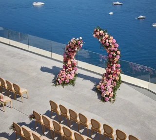 Cérémonie de mariage en bord de mer avec arches fleuries et rangées de chaises surplombant l’océan avec yachts au loin.