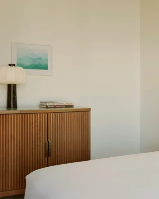 Bedroom detail showing cabinet with lamp and books, wall art, and bedside table with yellow roses.
