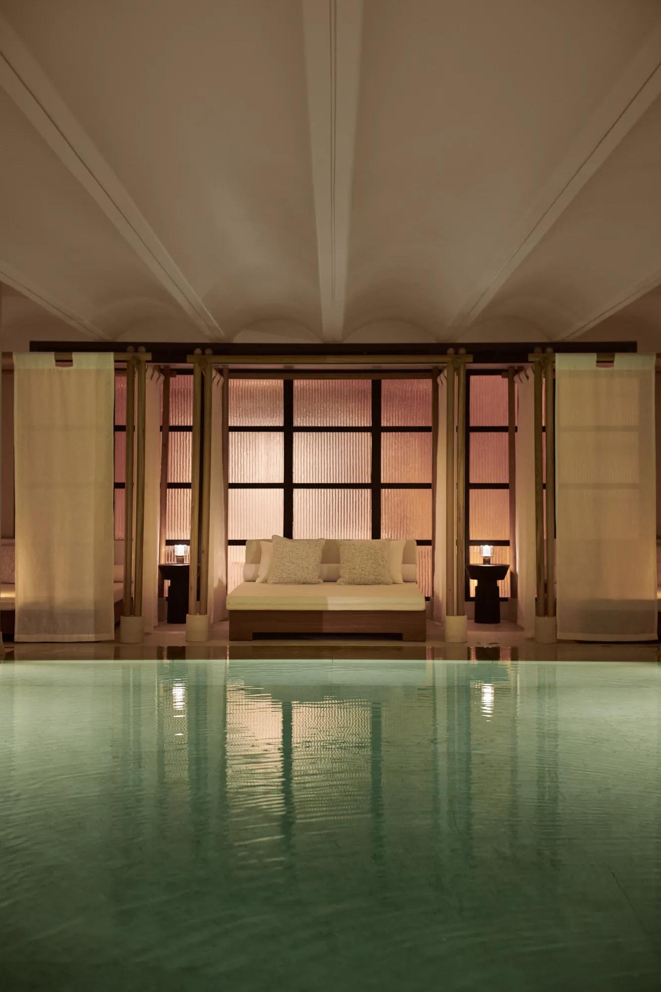 Serene indoor pool with daybed seating, soft lighting, and tranquil spa setting.