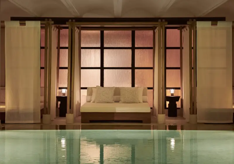 Serene indoor pool with daybed seating, soft lighting, and tranquil spa setting.