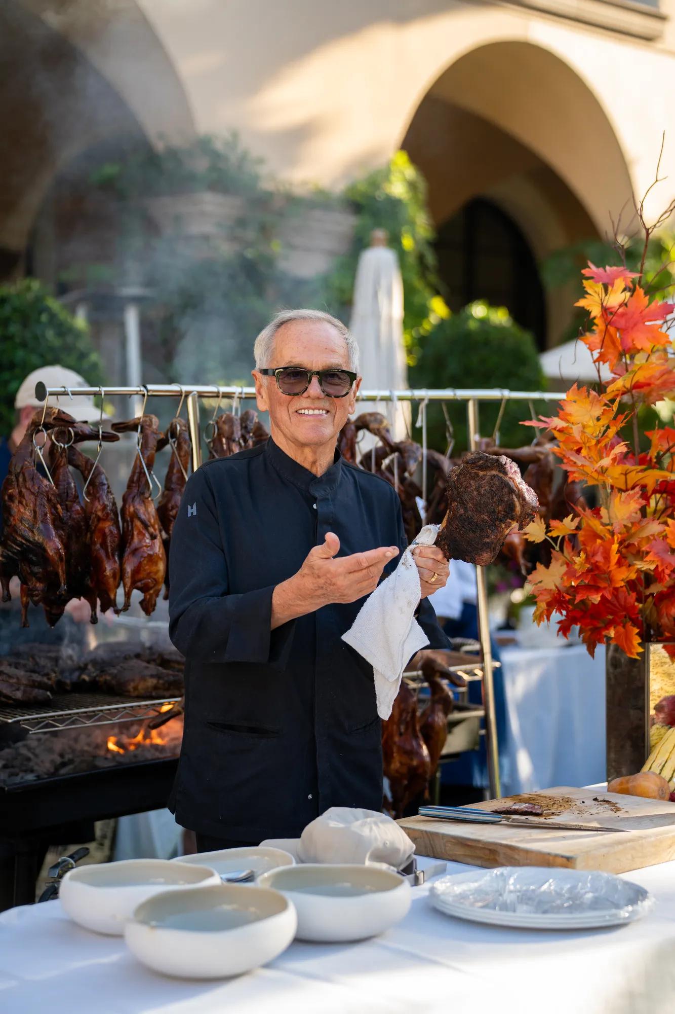 Chef carving smoked meat beside a live-fire grill decorated with autumn foliage.