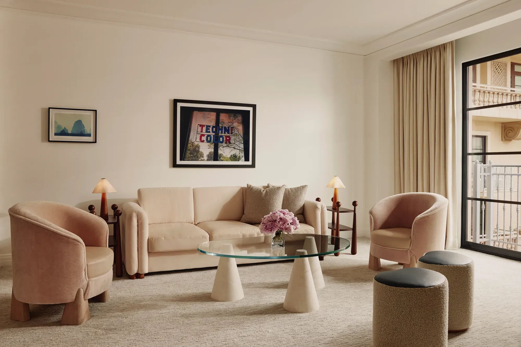 Soft‑toned living room with cream sofa, two pink armchairs, glass coffee table, and door to a balcony.