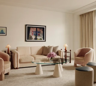 Soft‑toned living room with cream sofa, two pink armchairs, glass coffee table, and door to a balcony.