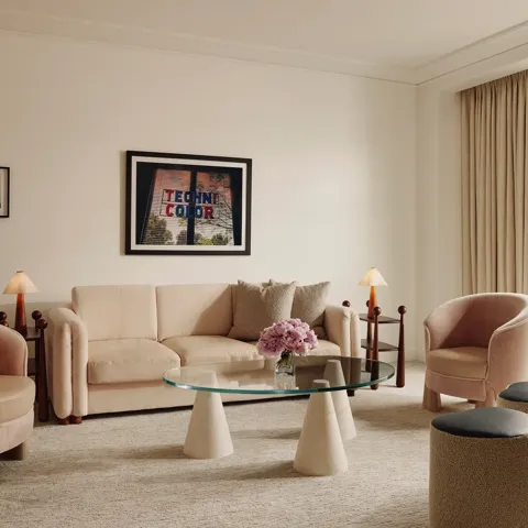 Soft‑toned living room with cream sofa, two pink armchairs, glass coffee table, and door to a balcony.
