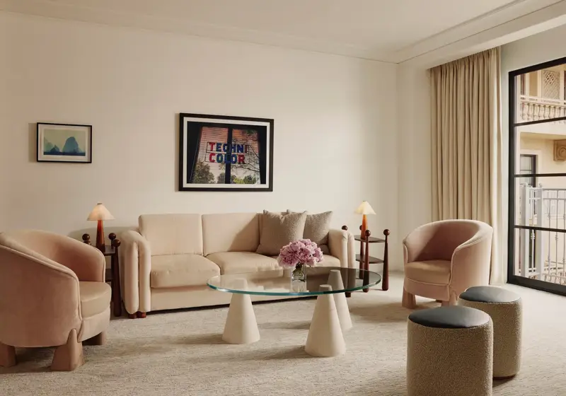 Soft‑toned living room with cream sofa, two pink armchairs, glass coffee table, and door to a balcony.