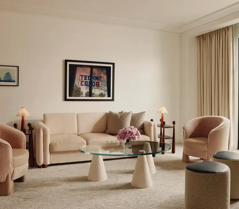 Soft‑toned living room with cream sofa, two pink armchairs, glass coffee table, and door to a balcony.