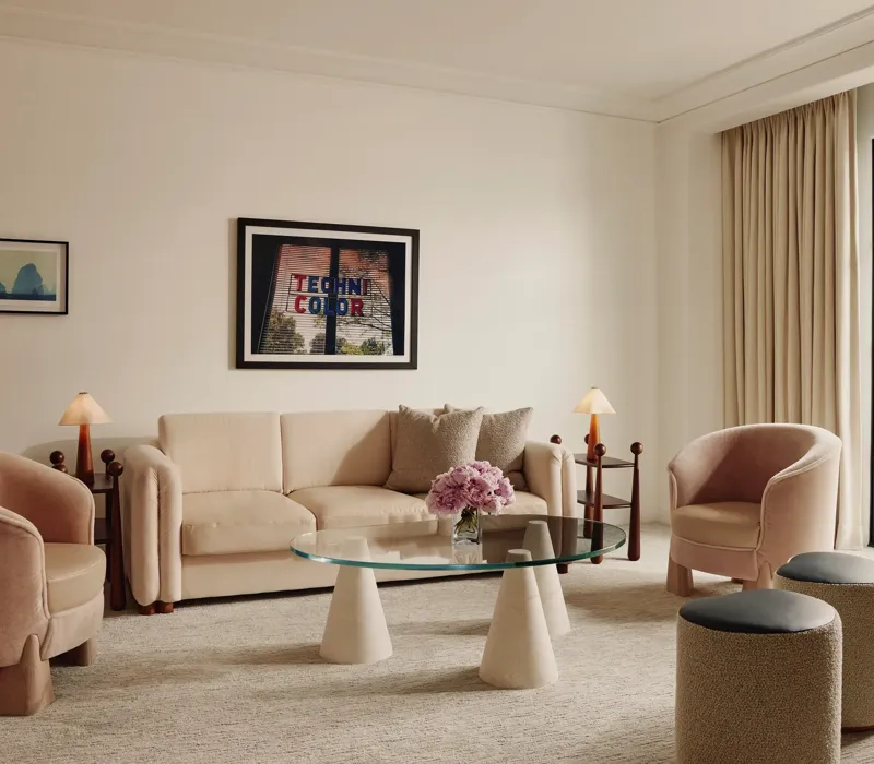 Soft‑toned living room with cream sofa, two pink armchairs, glass coffee table, and door to a balcony.