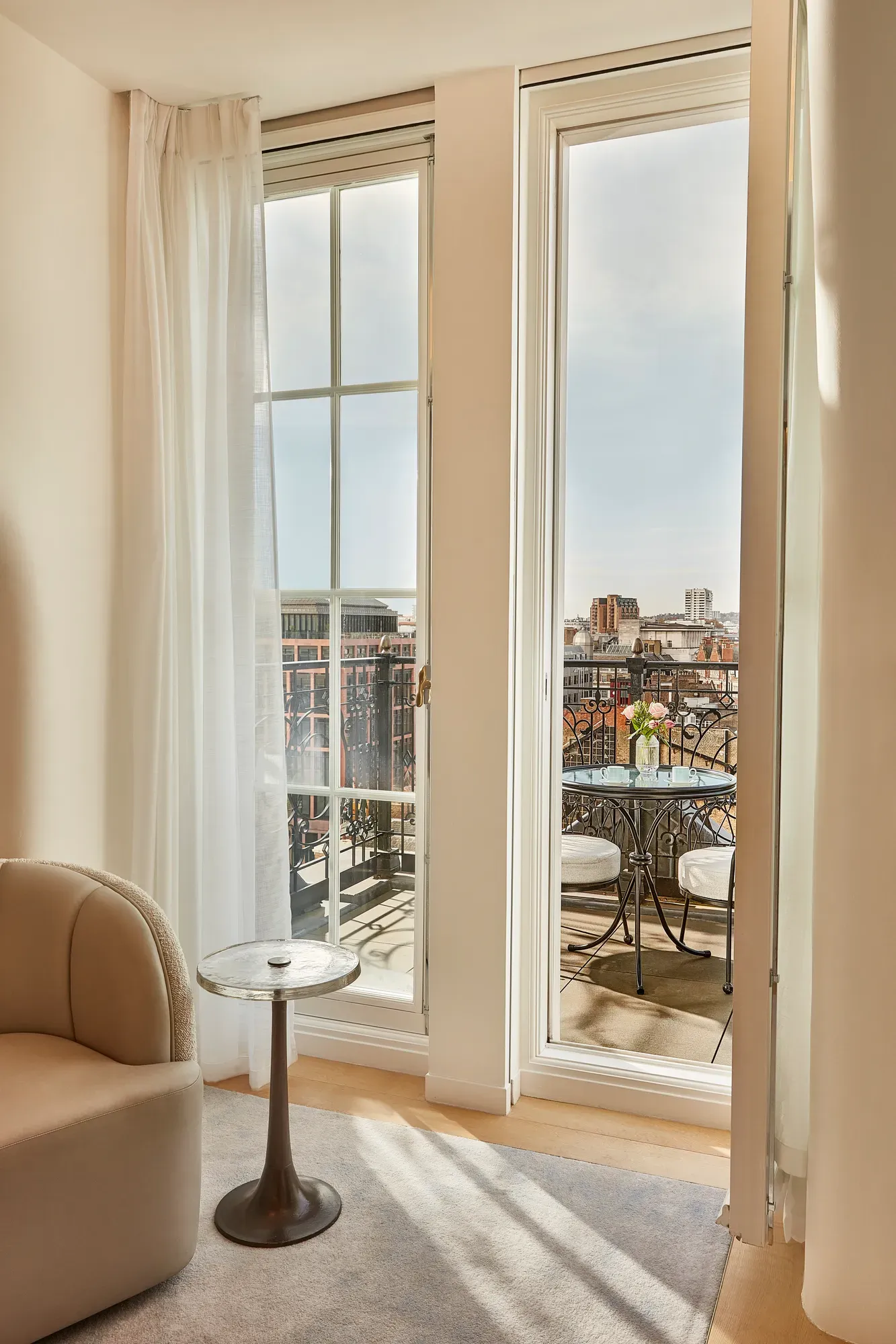 Floor-to-ceiling doors opening to balcony with table, chairs, and city skyline view.