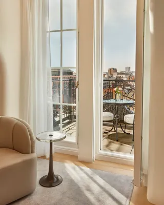 Floor-to-ceiling doors opening to balcony with table, chairs, and city skyline view.