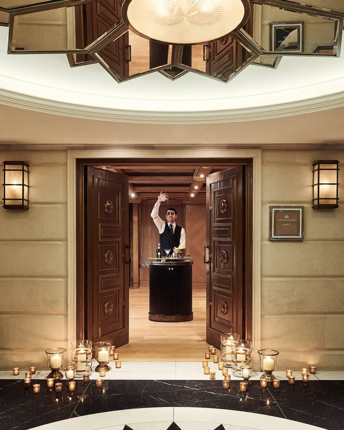 Candle-lit entrance with open double doors leading to a server presenting champagne in an elegant hallway.
