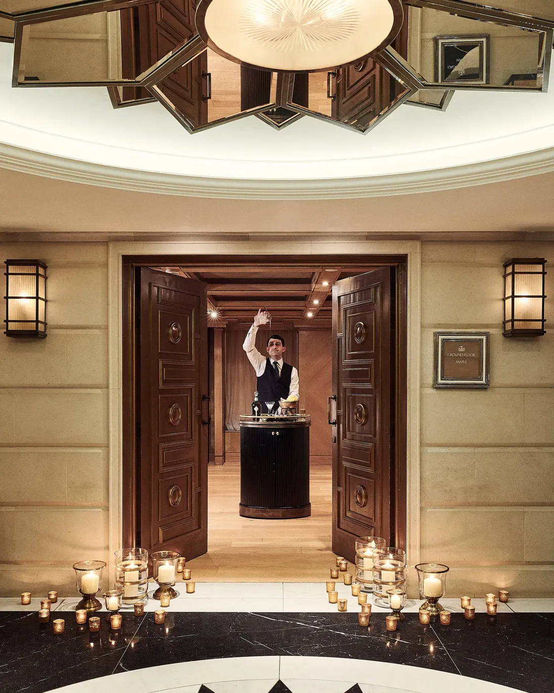 Candle-lit entrance with open double doors leading to a server presenting champagne in an elegant hallway.