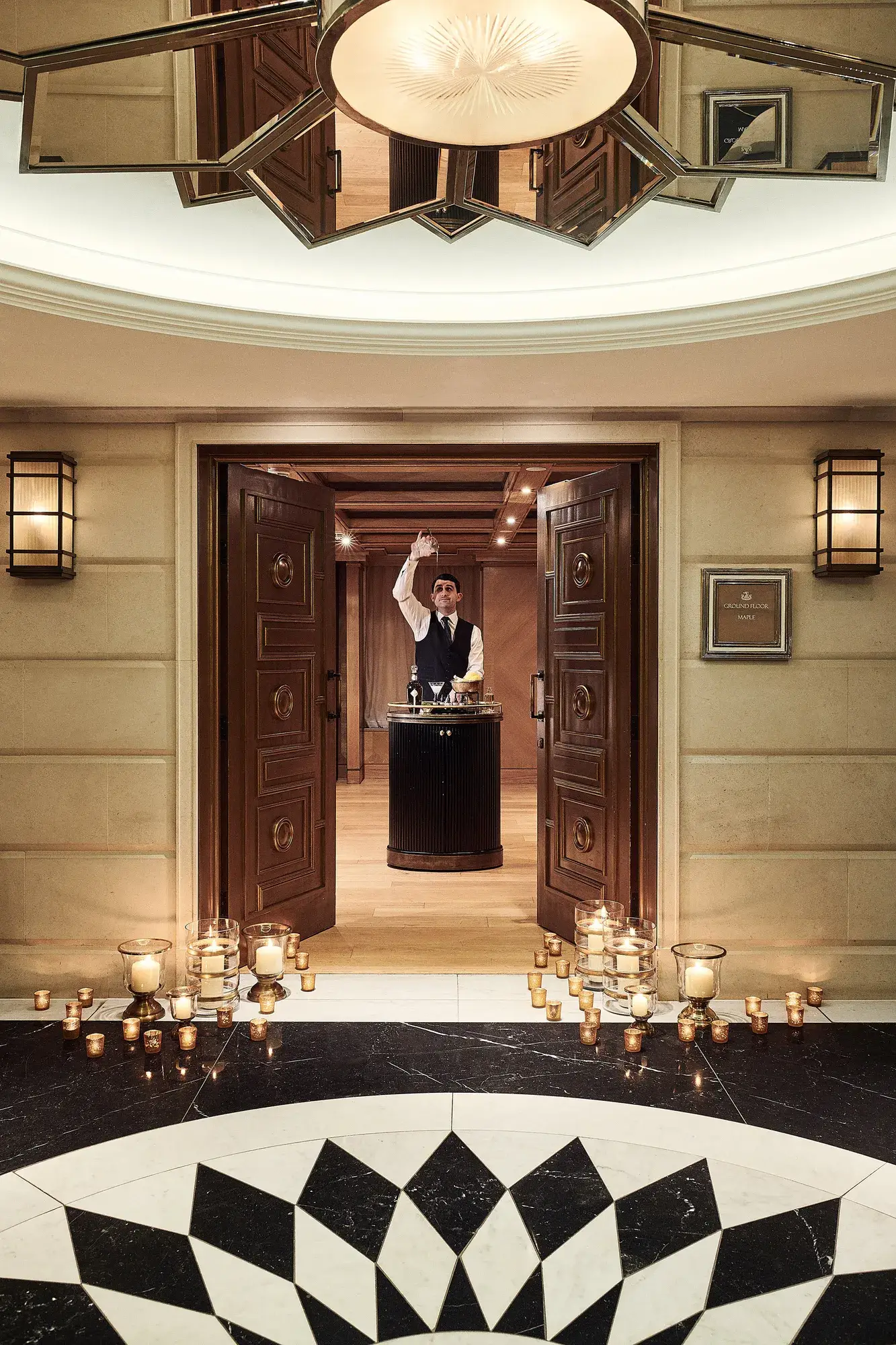 Candle-lit entrance with open double doors leading to a server presenting champagne in an elegant hallway.