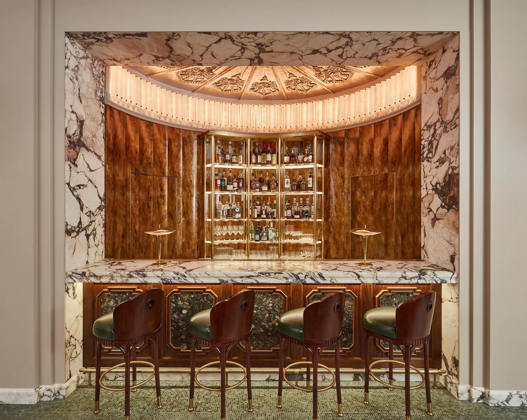 Art Deco bar with marble counter, wooden paneling, and four leather bar stools.