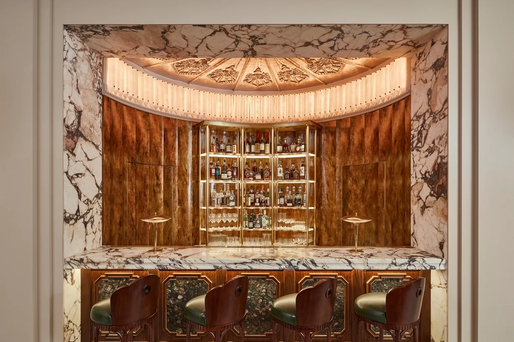 Art Deco bar with marble counter, wooden paneling, and four leather bar stools.