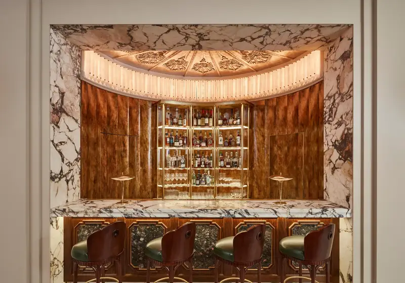 Art Deco bar with marble counter, wooden paneling, and four leather bar stools.