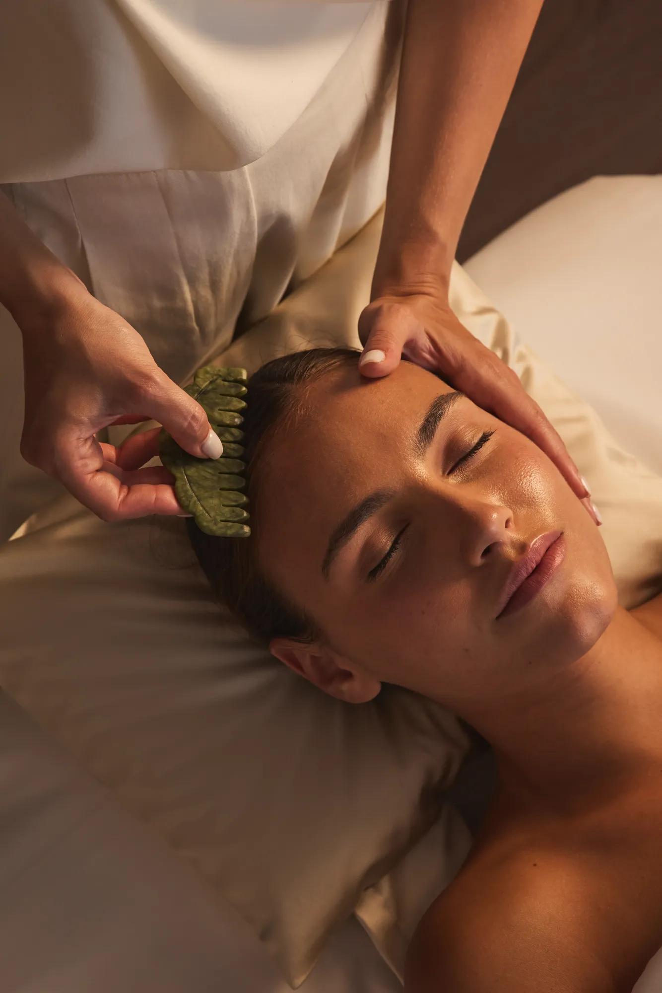 Gros plan d’un soin du visage, praticienne utilisant un gua sha en jade sur le front d’une cliente.