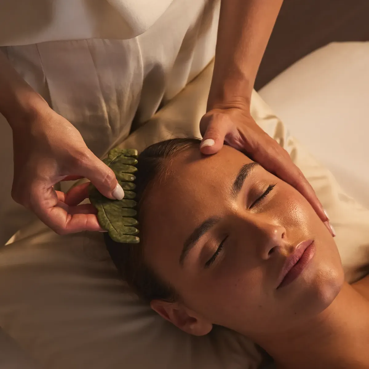Gros plan d’un soin du visage, praticienne utilisant un gua sha en jade sur le front d’une cliente.