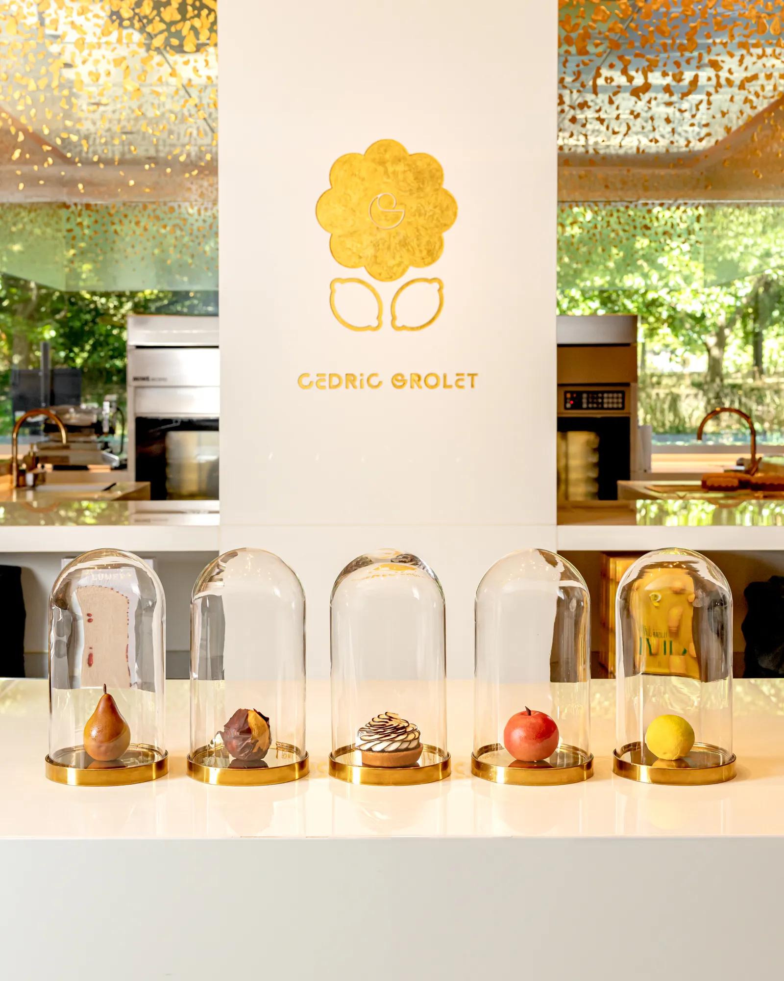 A selection of cakes sitting on a countertop with a Cedric Grolet sign behind it 