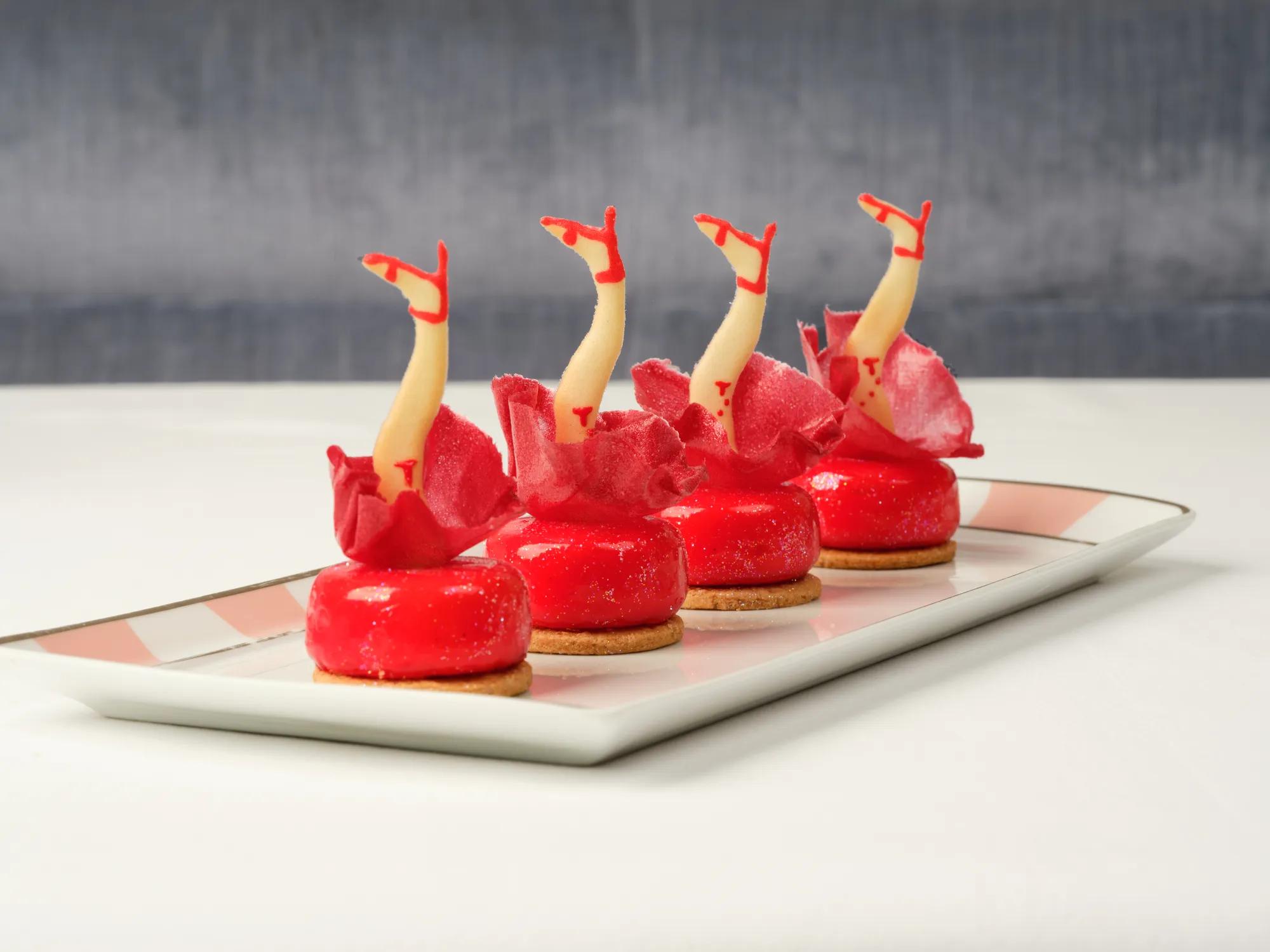 Four red pastries topped with decorative legs in red heels arranged in a row on a tray.