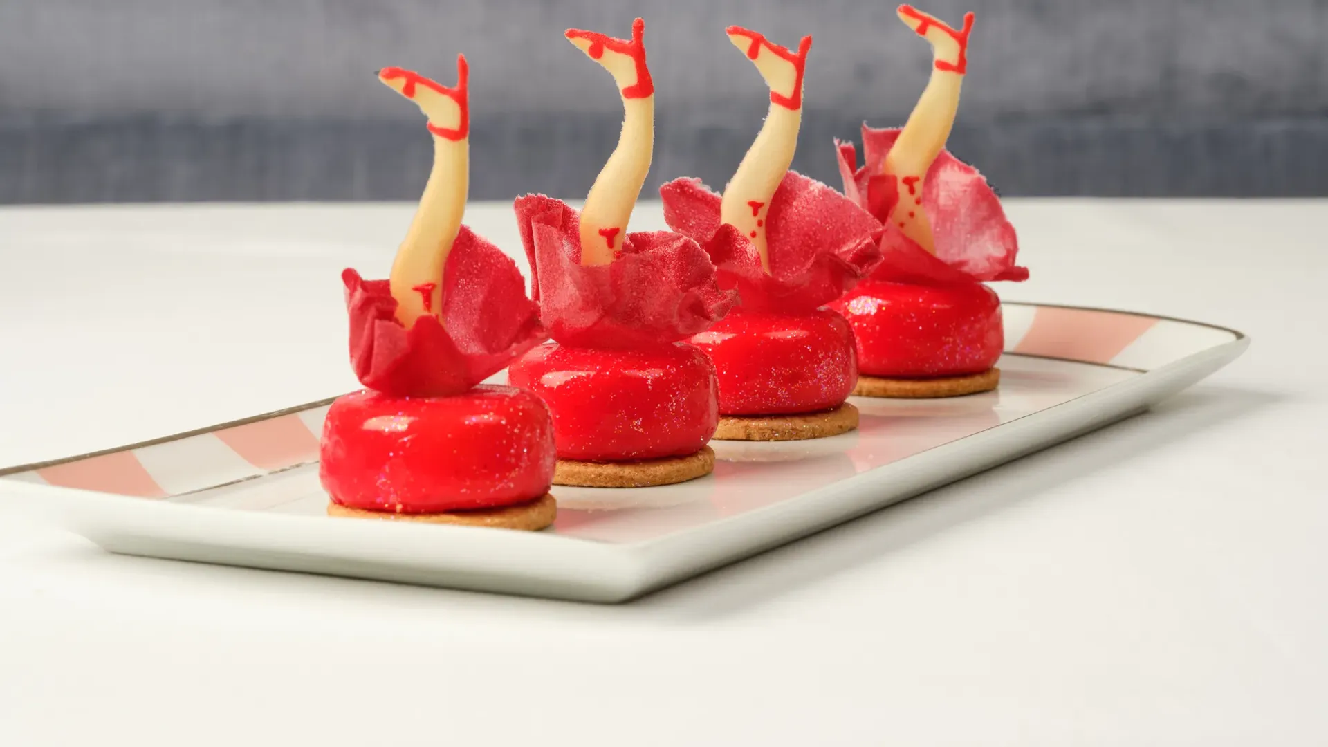 Four red pastries topped with decorative legs in red heels arranged in a row on a tray.