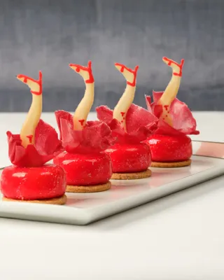 Four red pastries topped with decorative legs in red heels arranged in a row on a tray.