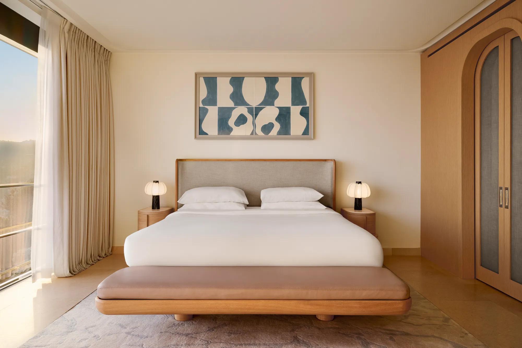 Chambre contemporaine avec grand lit, banc rembourré et œuvre abstraite au-dessus, complétée par des finitions en bois chaleureux et un éclairage doux.