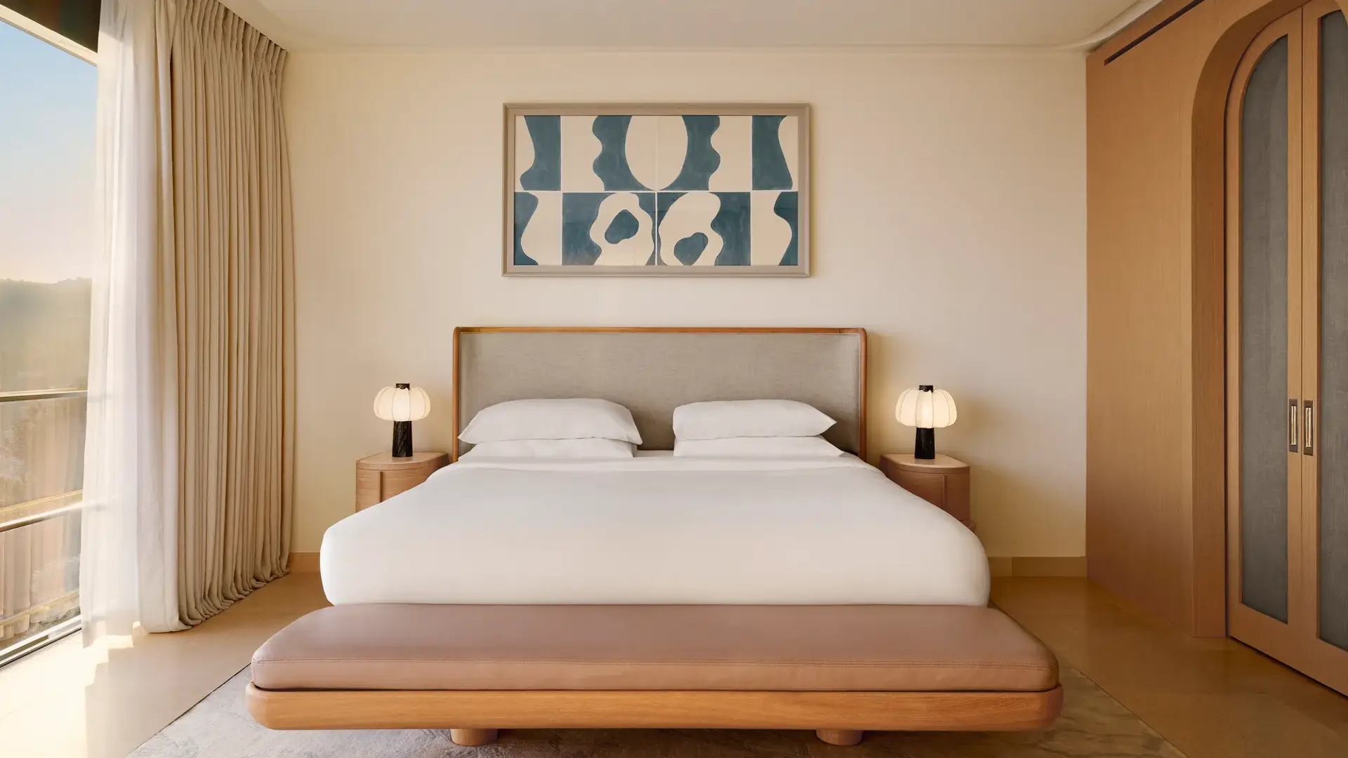 Chambre contemporaine avec grand lit, banc rembourré et œuvre abstraite au-dessus, complétée par des finitions en bois chaleureux et un éclairage doux.